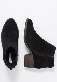 Mustat mokkanahkaiset nilkkurit, joissa pyöreä kärki, sivuvetoketju ja matala, pinoitu puukorko. Sileä pinta ja minimalistinen design.