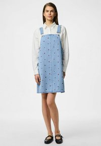 Hele sinine teksatükkidest kleit, millel on roosad lillemustrid, reguleeritavad rihmad ja sirge lõige. Kanduval valge pluusi peal.