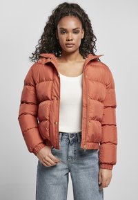 Polstret orange jakke med glidelås og trykknap-lukking, som har hette, ribbestrikkede ermer og en glatt, skinnenede tekstur. Uformell design med sidelommer.