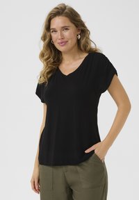 T-shirt noir à manches courtes en V fait d'un matériau doux, avec une coupe décontractée et des coutures latérales discrètes, associé à un pantalon vert olive.