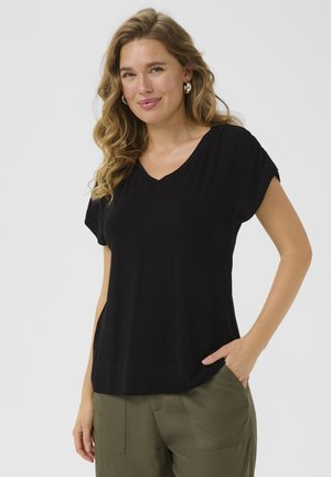 T-shirt noir à manches courtes en V fait d'un matériau doux, avec une coupe décontractée et des coutures latérales discrètes, associé à un pantalon vert olive.