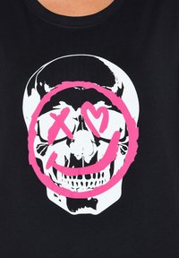 Camiseta negra con un gráfico central de una calavera en blanco, rodeada por una cara sonriente rosa con acentos de ojos en forma de 'X' y corazones.
