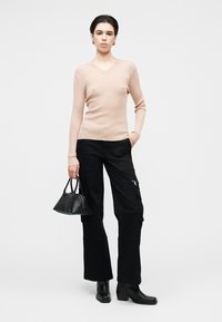 Pull côtelé beige clair à col en V, associé à un pantalon cargo noir avec poches latérales, des bottines et un petit sac à main noir.