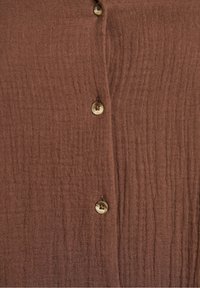 Brauner, strukturierter Stoffoberteil mit vertikalen Rippungen, ausgestattet mit vier runden Knöpfen in einer hellen Sandfarbe entlang der Vorderseite.