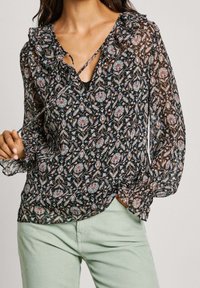 Zwarte bloemenblouse met gerimpelde halslijn, lange doorschijnende mouwen en een strikdetail aan de voorkant; voorzien van een kleurrijk, ingewikkeld patroon.