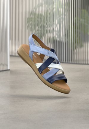 Sandale en cuir bleue et blanche avec des brides croisées, une semelle intérieure rembourrée beige et une semelle en bois clair. Texture lisse et design moderne.