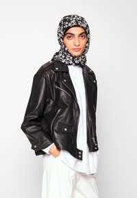 Jaqueta de moto de couro preta com acessórios em prata. Combinada com uma camisa branca e um lenço de cabeça preto com padrão floral. Corte descontraído, design angular.
