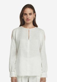 Blusa bianca in lino con maniche lunghe, scollatura rotonda, dettaglio a chiave sul davanti e tagli laterali. Tessuto morbido e testurizzato.