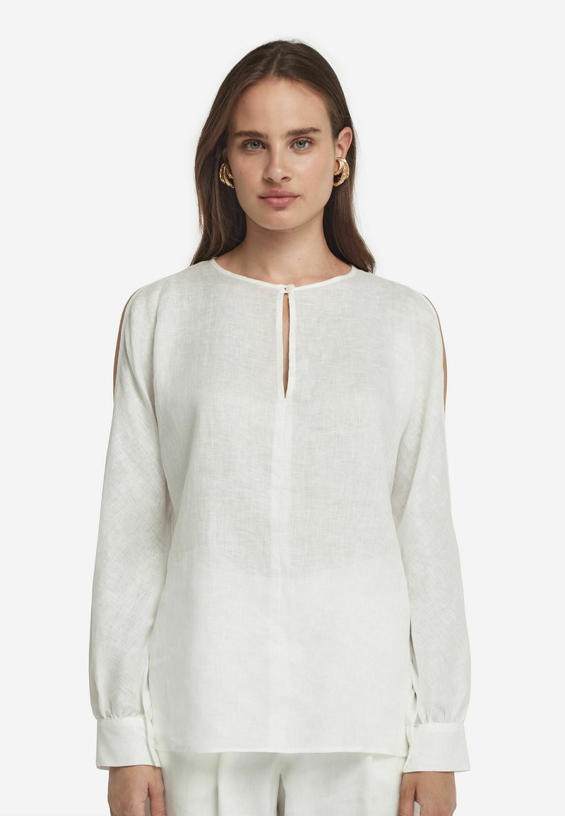 Blusa bianca in lino con maniche lunghe, scollatura rotonda, dettaglio a chiave sul davanti e tagli laterali. Tessuto morbido e testurizzato.