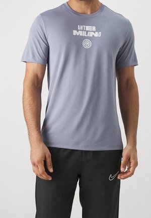 Homme portant un maillot de sport Inter Milan à manches courtes gris clair et un short noir Nike, debout les bras détendus le long du corps.