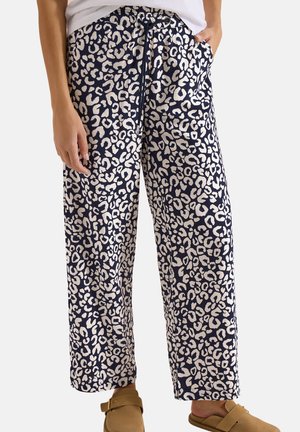 Pantalon imprimé léopard bleu marine et blanc avec taille à cordon, porté avec des chaussures beige à enfiler et un haut blanc.