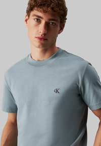 Camiseta de manga corta azul claro, hecha de una tela suave, con cuello redondo y un pequeño logo bordado en el lado izquierdo del pecho.