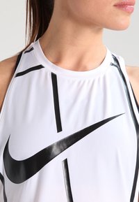 Canottiera atletica bianca con design geometrici neri e un prominente logo Nike swoosh nero. Tessuto liscio e leggero.
