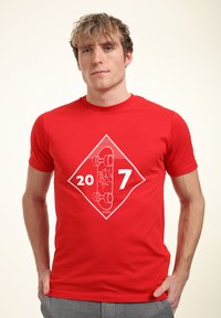 Rød bomulds T-shirt med en hvid grafik af et skateboard inden for en diamantform, med numrene "20" og "7" nedenfor.