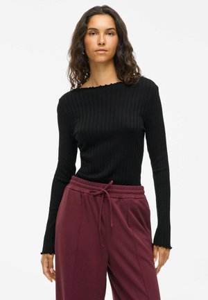 Haut noir à manches longues avec un col bateau et des bords festonnés, associé à un pantalon bordeaux avec cordon de serrage, en tissu doux.