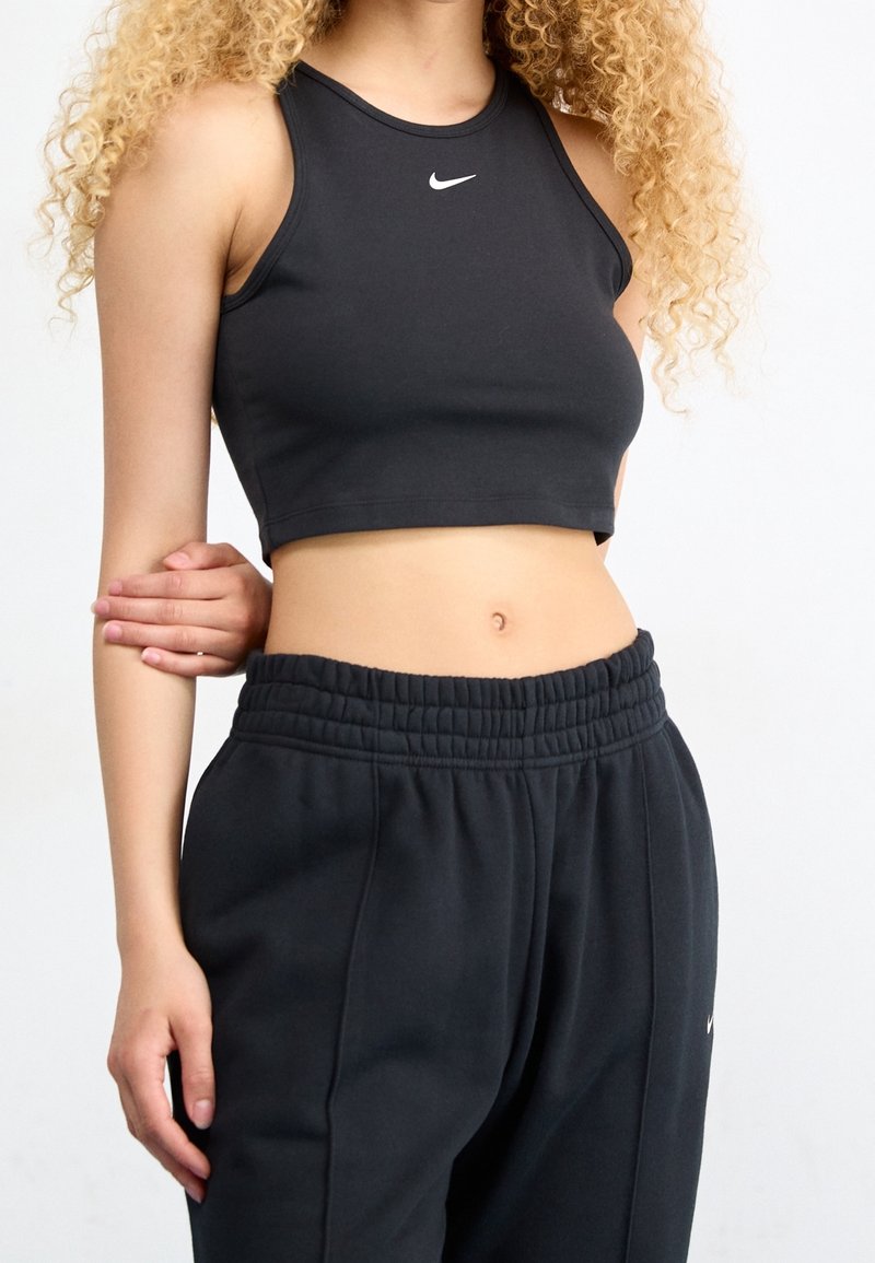 Un top court noir à encolure ronde avec le logo Nike sur la poitrine, associé à un pantalon de survêtement noir ample avec une taille élastique.