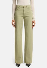 Lichtgroene wijde broek van een zachte stof. Voorzien van voorzakken, een knoopsluiting en een hoge taille, gecombineerd met zwarte studschoenen.