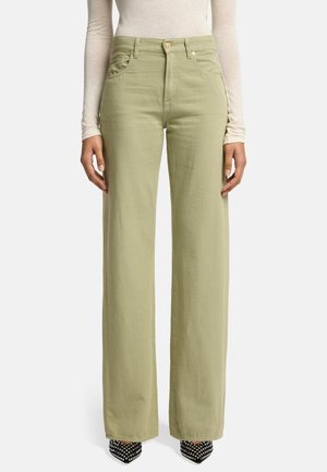 Lichtgroene wijde broek van een zachte stof. Voorzien van voorzakken, een knoopsluiting en een hoge taille, gecombineerd met zwarte studschoenen.