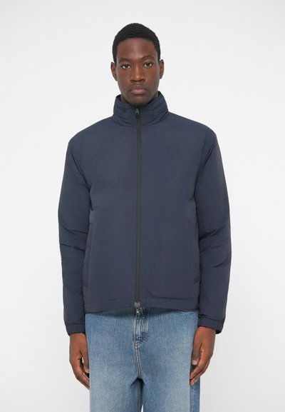 Chaqueta acolchada de color azul marino con cuello alto, cierre frontal completo y bolsillos laterales. Tela suave y ligera con detalles de costura mínimos.