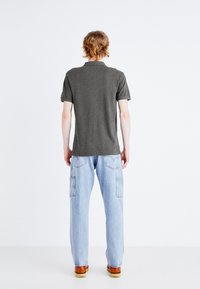 Polo shirt gris à manches courtes, associé à un pantalon cargo léger bleu clair avec des poches. Le mannequin se tient de dos contre un fond neutre.