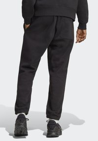 I pantaloni tuta neri presentano un design affusolato con polsini in coste alle caviglie e una tasca posteriore. Il tessuto è morbido, offrendo una vestibilità casual e confortevole.