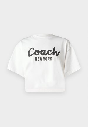 Bijela skraćena majica od pamuka, s podebljanim crnim natpisom "Coach New York" smještenim u središtu prednje strane. Kratki rukavi i okrugli izrez.