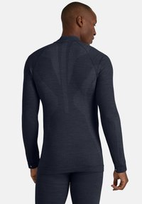 Koszula z długim rękawem w ciemnoszarym materiale z teksturowanymi wzorami i dopasowanym krojem. Posiada wysoki kołnierz oraz otwory na kciuki na końcach rękawów.