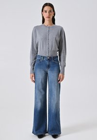 Grauer Button-Up-Cardigan mit geripptem Saum, kombiniert mit hoch taillierten, weit geschnittenen blauen Jeans aus Denim mit leichter Ausbleichung und klassischen Taschen.