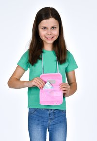 Una borsa rosa trasparente con una tracolla, tenuta da un bambino. All'interno c'è una scheda con testo visibile. Il bambino indossa una maglietta verde e jeans di denim.