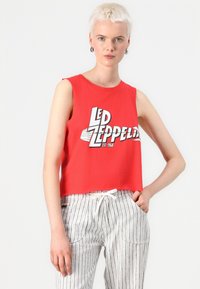 Red sleeveless crop top featuring a Led Zeppelin graphic, made from cotton. Paired with striped, drawstring trousers in gray and white.