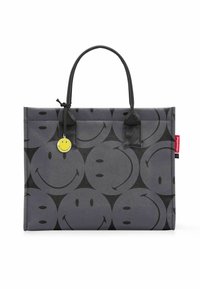 Borsa tote grigia con un motivo di faccine sorridenti ripetuto, dalla texture opaca, manici neri e un charm a forma di faccina sorridente gialla su un lato.