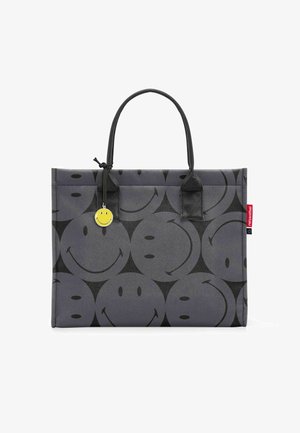 Grijze tote bag met een herhalend patroon van glimlachen, met een matte textuur, zwarte handvatten en een gele glimlachcharme aan de zijkant.