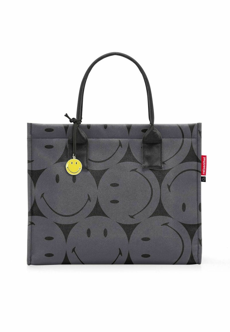 Borsa tote grigia con un motivo di faccine sorridenti ripetuto, dalla texture opaca, manici neri e un charm a forma di faccina sorridente gialla su un lato.