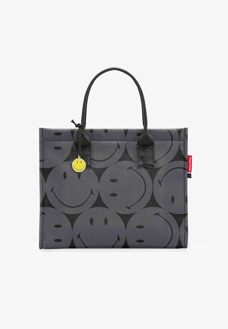Grijze tote bag met een herhalend patroon van glimlachen, met een matte textuur, zwarte handvatten en een gele glimlachcharme aan de zijkant.