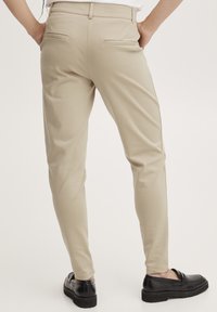 Beiga slim-fit byxor med en slät textur och två bakfickor. Bärs med svarta loafers som har en lätt klack och rund tå.