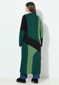 Langer Strickcardigan mit geometrischem Muster in Dunkelgrün, Hellgrün und Schwarz. Strukturiertes Material mit lockerer Passform und langen Ärmeln.