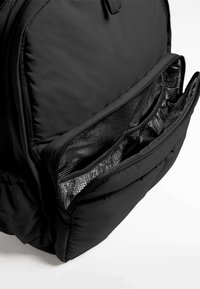 Poche avant isolée noire d'un sac à dos ouverte, montrant les compartiments organiseurs en mesh à l'intérieur.