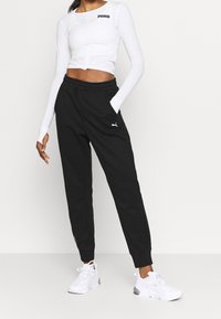 Zwarte sweatpants met zijzakken en een wit Puma-logo; gecombineerd met een strakke witte longsleeve top en witte sport sneakers.