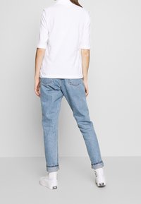 White short-sleeve polo shirt paired with light blue relaxed-fit jeans and white sneakers, featuring rolled-up cuffs for a casual look.