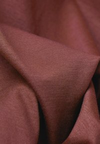 Bordowy materiał o miękkiej, gładkiej fakturze, z fałdami i marszczeniami, które podkreślają jego ciężar i elastyczność.