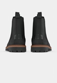 Melnas ādas potīšu zābaki ar teksturētu virsmu, cilpām vilkšanai un kontrastējošām brūnām gumijas zolēm ar dziļu protektoru. Sānos uzlīmes.