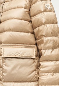 Μπεζ puffer μπουφάν με ομαλή, γυαλιστερή υφή. Διαθέτει οριζόντια ραμμένες τμήματα και τσέπη με μεταλλική κεντημένη λογότυπο στο μπροστινό μέρος.