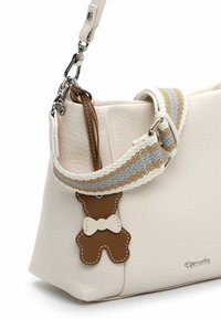 Kremowa torebka wykonana z fakturowanej skóry, z wielopasmowym, tkanym paskiem oraz zawieszką w kształcie misia w kolorach brązowym i białym.