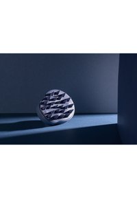 Rund, mørkeblå genstand med et tekstureret, forhøjet overflademønster, der ligner en række toppe; fremstillet af et glat materiale.