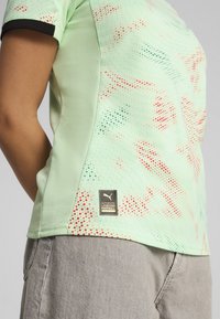 Maillot de football Puma vert menthe en tissu respirant, avec un motif à pois et des accents rouges, et un col noir. Comprend une étiquette de logo.