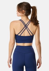 Top sportivo blu navy con spalline incrociate, texture liscia e dettagli con logo. Abbinato a leggings a vita alta coordinati.