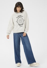 Hellgraue Sweatshirt mit floralem Druck und Text. Kombiniert mit weiten, dunkelblauen Jeans und weißen Sneakers. Weiche Stofftextur, lässige Passform.
