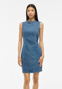 Robe en denim sans manches, avec un col montant, design ajusté, longueur mi-cuisse et coutures contrastées. Couleur bleu clair, texture lisse.