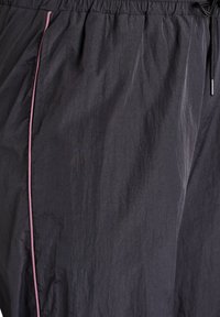 Dunkelgrauer Stoff mit leichten Falten, pinke Paspel entlang der Seitennaht und schwarzer elastischer Bund mit sichtbarer Kordelspitze.