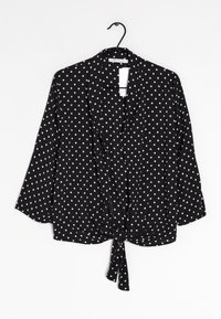 Svart blus med prickar, trekvartsärmar, knyt-fram design och lättviktig textil. Vita prickar jämnt fördelade över tyget.